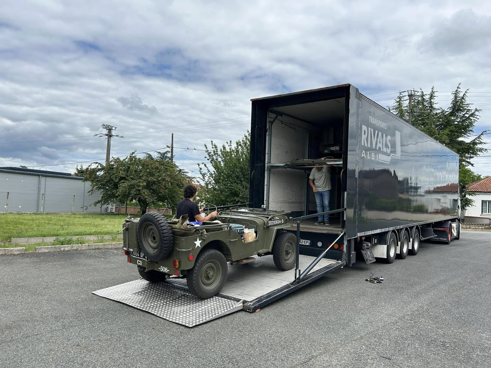Petit véhicule militaire en train d'être chargé dans un camion des Transports Rivals